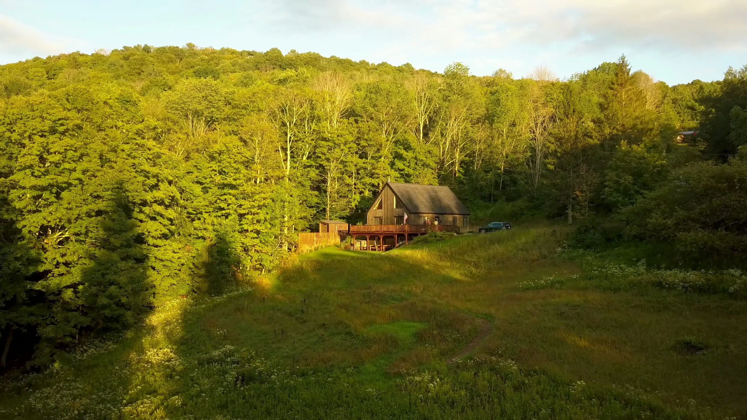 Golden-hour aerial of Evergreen Overlook — the A-frame cabin and wraparound deck glowing in evening light against nine wooded acres