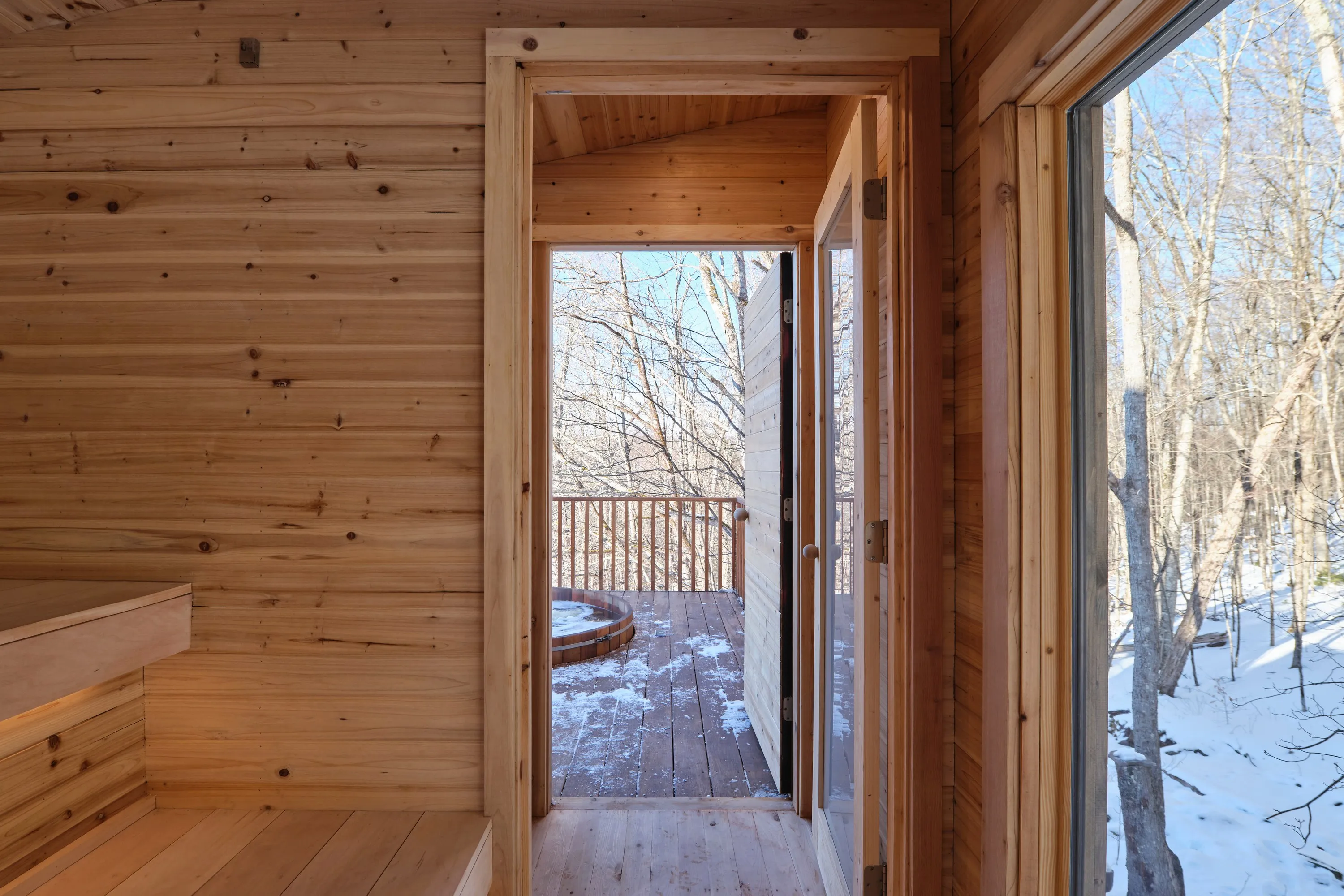 Inside the custom cedar sauna, the door open to the deck and the cedar hot tub beyond